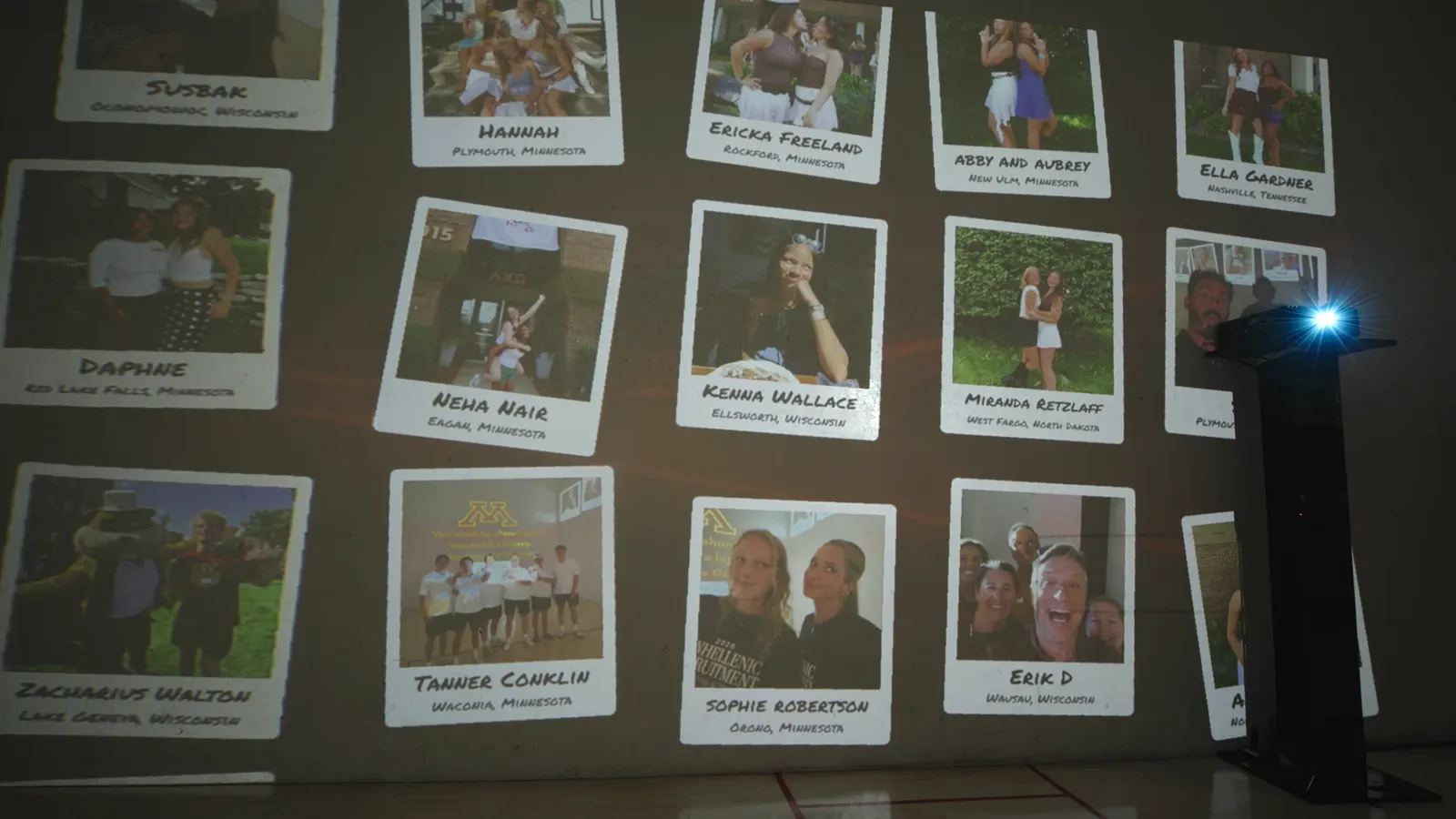 A projected wall of instant-photo frames, each with a new student’s name and hometown.
